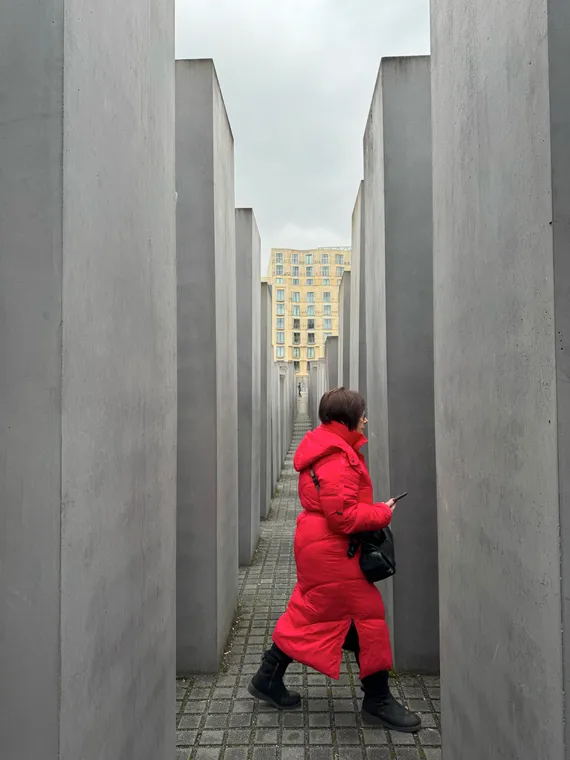 The Memorial for the Murdered Jews of Europe, a field of many gray concrete slabs of varying heights. A woman in a long red coat passes between them, a short distance from the camera.