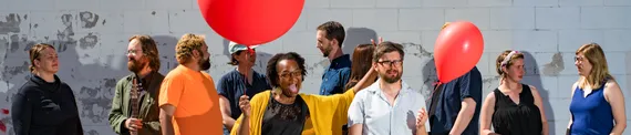 A bunch of improvisers expressing different emotions, two of them holding red balloons.