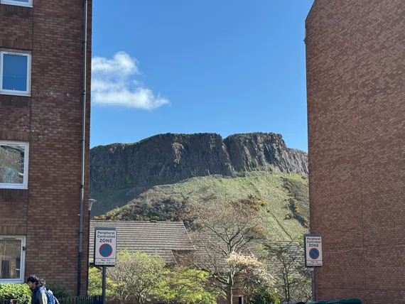 Arthur's Seat, a green hill capped by craggy rock, seen through a narrow gap between apartment buildings.
