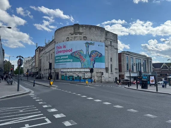 An enormous sign on a curved building reads 'This is Liverpool: open, proud and welcoming', with a painting of a bird.