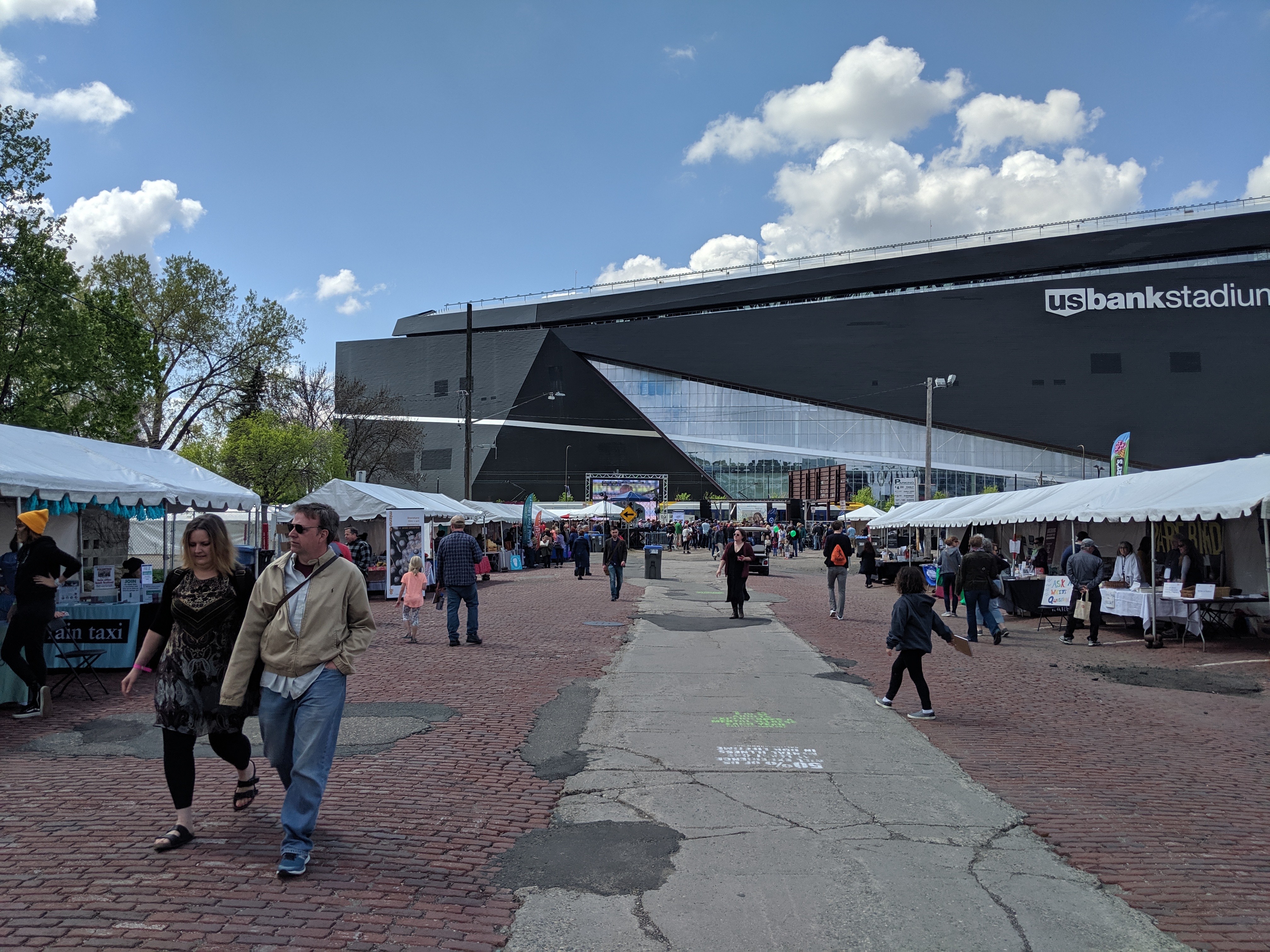 People walking past booths at the Wordplay festival, with US Bank Stadium looming over the scene.